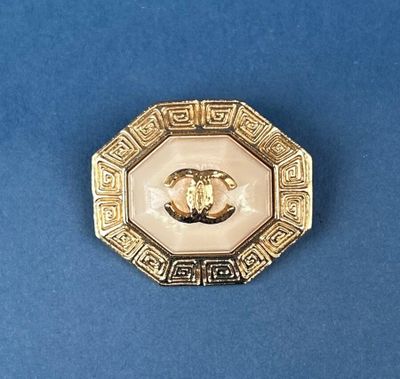 an image of a gold and white broochle on a blue surface
