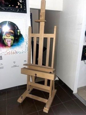 un chevalet en bois sur lequel est posé un tableau, devant une affiche