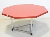 une petite table au plateau rouge posée sur un sol blanc