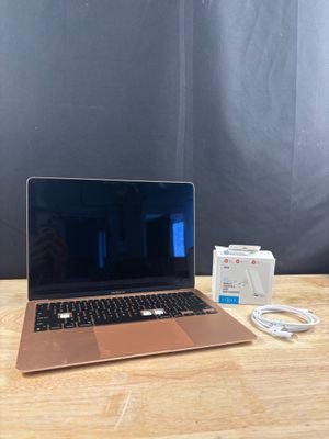 un ordinateur portable Apple posé sur une table en bois, à côté d'un chargeur