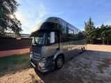 a silver bus parked in a parking lot with trees in the background