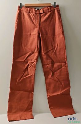 an orange pants hanging on a hanger against a wall