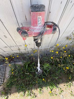 une perceuse rouge et noire posée par terre à côté d'un bâtiment