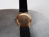 a gold watch with a black band on a white surface