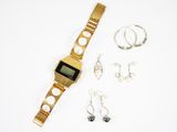 une montre en or et une paire de boucles d'oreilles posées sur une surface blanche