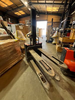 un chariot élévateur dans un entrepôt rempli de palettes et de cartons