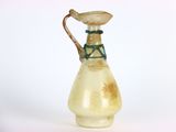 un petit vase en verre muni d'une anse, posé sur une surface blanche