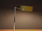 a green lamp on a wooden table with a black wall behind it