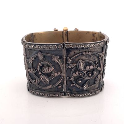 an antique silver bracelet with flowers and leaves on it