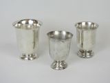 trois tasses en argent posées l'une à côté de l'autre sur une surface blanche