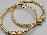 two gold bracelets with pearls on them on a white surface