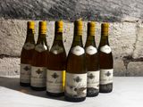 six bottles of wine are lined up on a table in front of a stone wall
