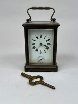 une petite horloge et une clé posées sur une surface blanche
