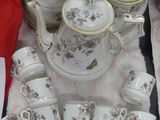 many cups and saucers on a table with a red cloth