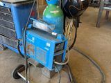 un chariot bleu sur lequel se trouve une bouteille verte, dans un garage