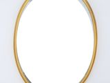 a round mirror with a gold frame on a white wall