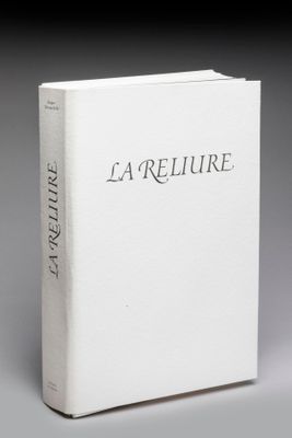 « La reliure », un ouvrage écrit par l'auteur du roman, est présenté sur une surface grise