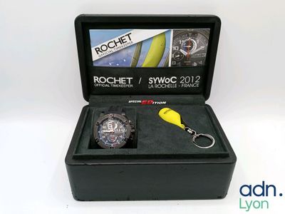 La montre est présentée dans un coffret noir avec un porte-clés jaune.