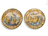 two decorative plates with figures on them on a white surface