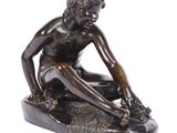 bronze statue of a boy sitting on a rock with his feet on the ground