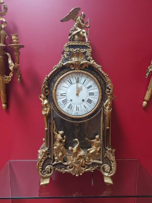 une horloge dorée posée sur une table en verre devant un mur rouge