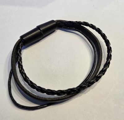 un gros plan d'un bracelet en cuir noir posé sur une surface blanche