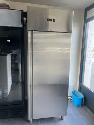 un réfrigérateur argenté dans une cuisine, devant lequel se trouve un seau bleu