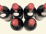 six bottles of wine are lined up in a row on a white surface
