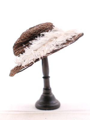 un chapeau marron orné de plumes blanches, posé sur un support noir