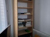 a desk with a computer and a book shelf in the corner