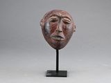 une image représentant un masque en bois posé sur un socle, sur fond gris