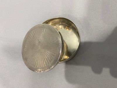 un petit récipient en argent posé sur une table, avec l'ombre d'une personne