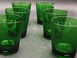 six green glasses are lined up on a counter top