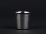 an empty metal cup on a black surface with a black background