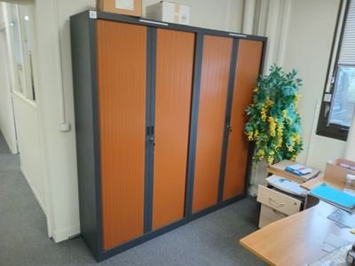 des casiers orange et noirs dans un bureau, avec une plante dans un coin