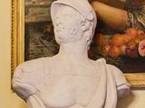 une statue représentant une femme tenant un fruit devant un tableau