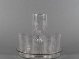 un pichet en verre transparent et des verres posés sur un plateau en argent