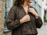 woman wearing a leopard print shirt and jeans standing in front of a brick building