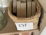 un panier rempli de livres posé sur une étagère, à côté d'un bocal contenant des bougies