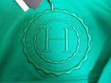 a close up of a green hoodie with the letter h on it