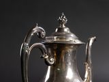 silver plated coffee pot with ornate handle on a black background