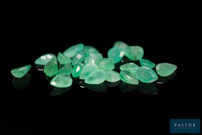 a close up of a pile of green emeralds on a black surface