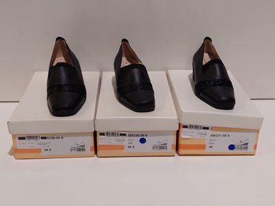 trois paires de chaussures noires posées sur des cartons, sur une surface blanche
