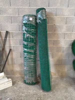 two rolls of green netting on the ground next to a brick wall