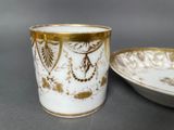 a white and gold cup sitting next to a plate