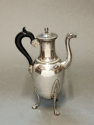 une théière ancienne en argent, dotée d'une anse noire, posée sur une table