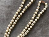 un collier de perles blanches muni d'un fermoir en or, sur fond gris