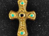 a gold cross with turquoise stones on it sitting on a black surface
