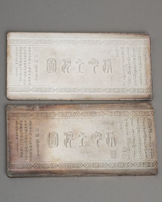 pair of chinese silver cigarette cases with writing on them on a gray surface