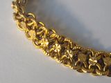 gold plated bracelet with flowers and stars on it on a white surface